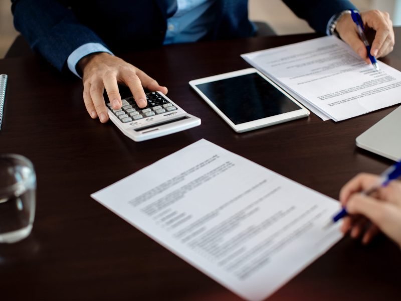 Close-up of real estate agent calculating costs of a mortgage agreement while having a meeting with a client in the office.